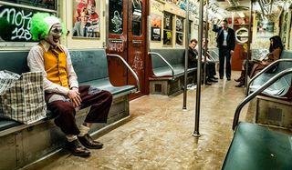 Joker Arthur laughing on the subway in his full clown outfit