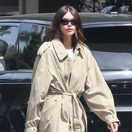 Kaia Gerber wearing a trench coat, a white T-shirt, navy satin pants, and red ballet flats