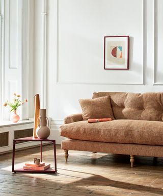 A living room with a brown couch, wall art, a table, and white walls