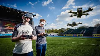 Two drone pilots, standing in a soccer field, flying FPV drones