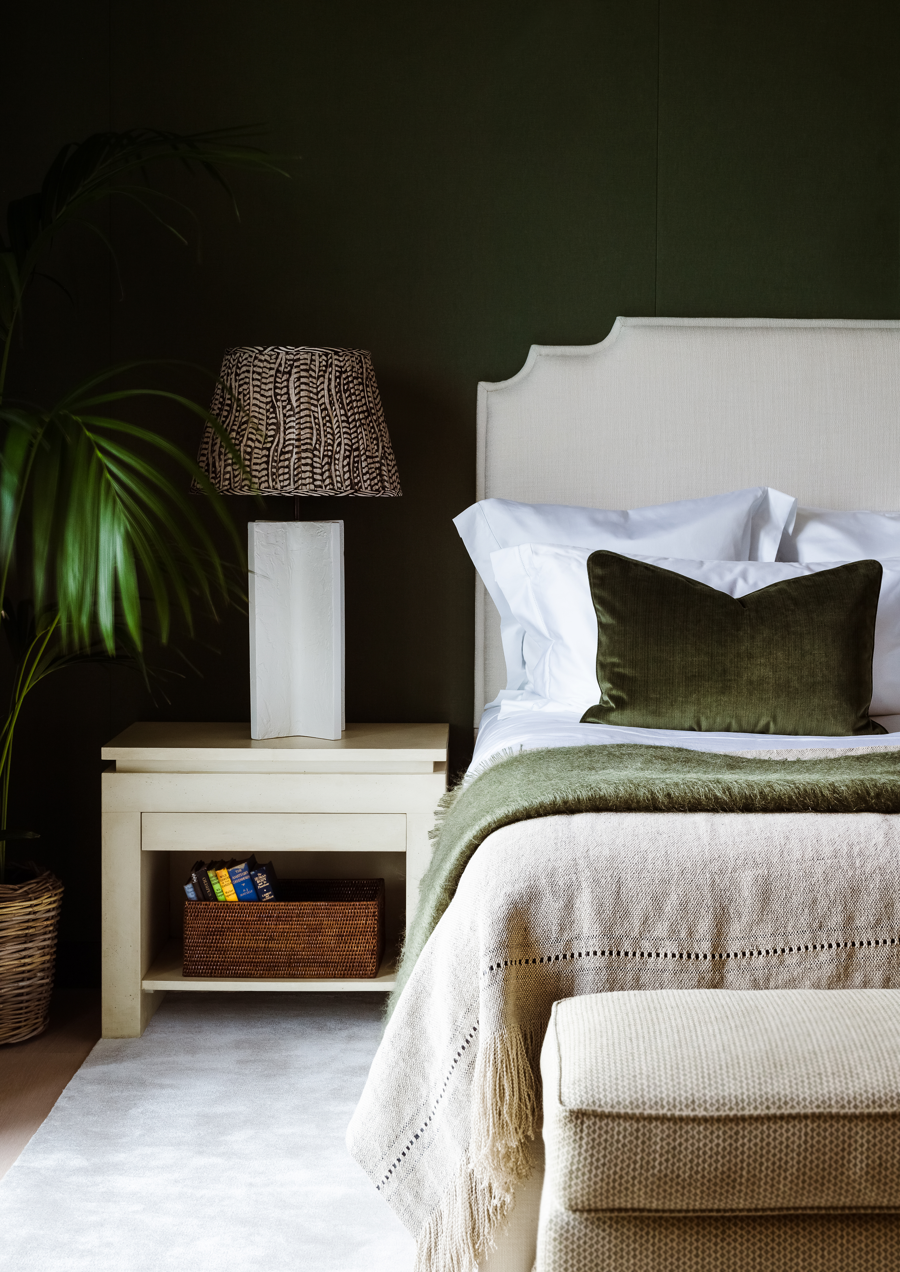 dormitorio verde oscuro con cama beige, tiro, otomano, alfombra, mesa auxiliar, pantalla de lámpara estampada, planta