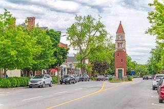 a small clocktower stands in the middle of a road lined with green trees.