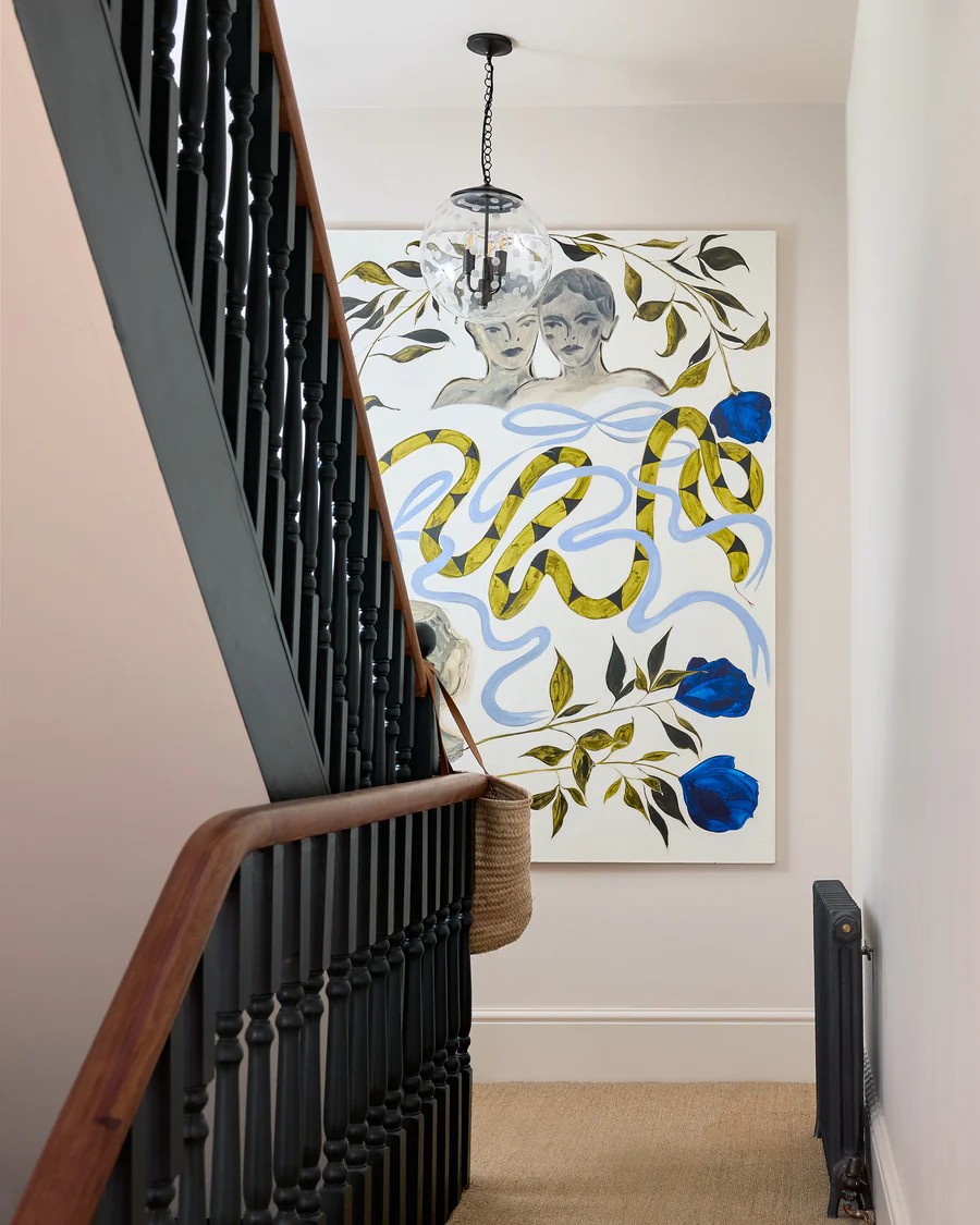 Image of a clear polkadot pendant light in a white stairwell with black railing. There is a large abstract painting on the wall.