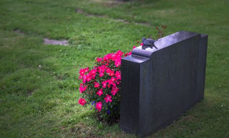 Black gravestone with spray of red flowers at base