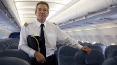 An airline pilot stands in the aisle of a plane.