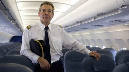 An airline pilot stands in the aisle of a plane.