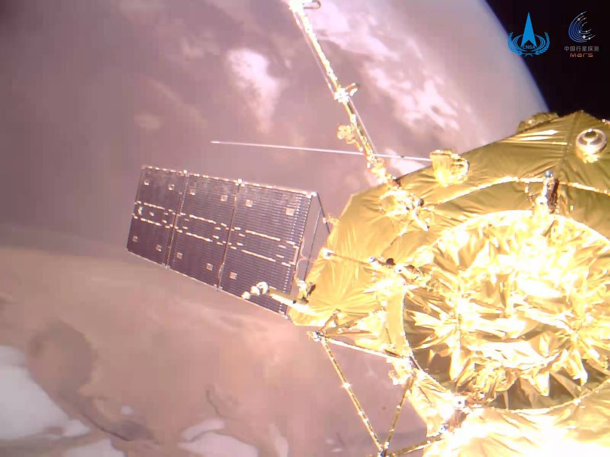 A closeup shot of the golden Tianwen 1 and its solar array and science antennae above Mars' north pole.