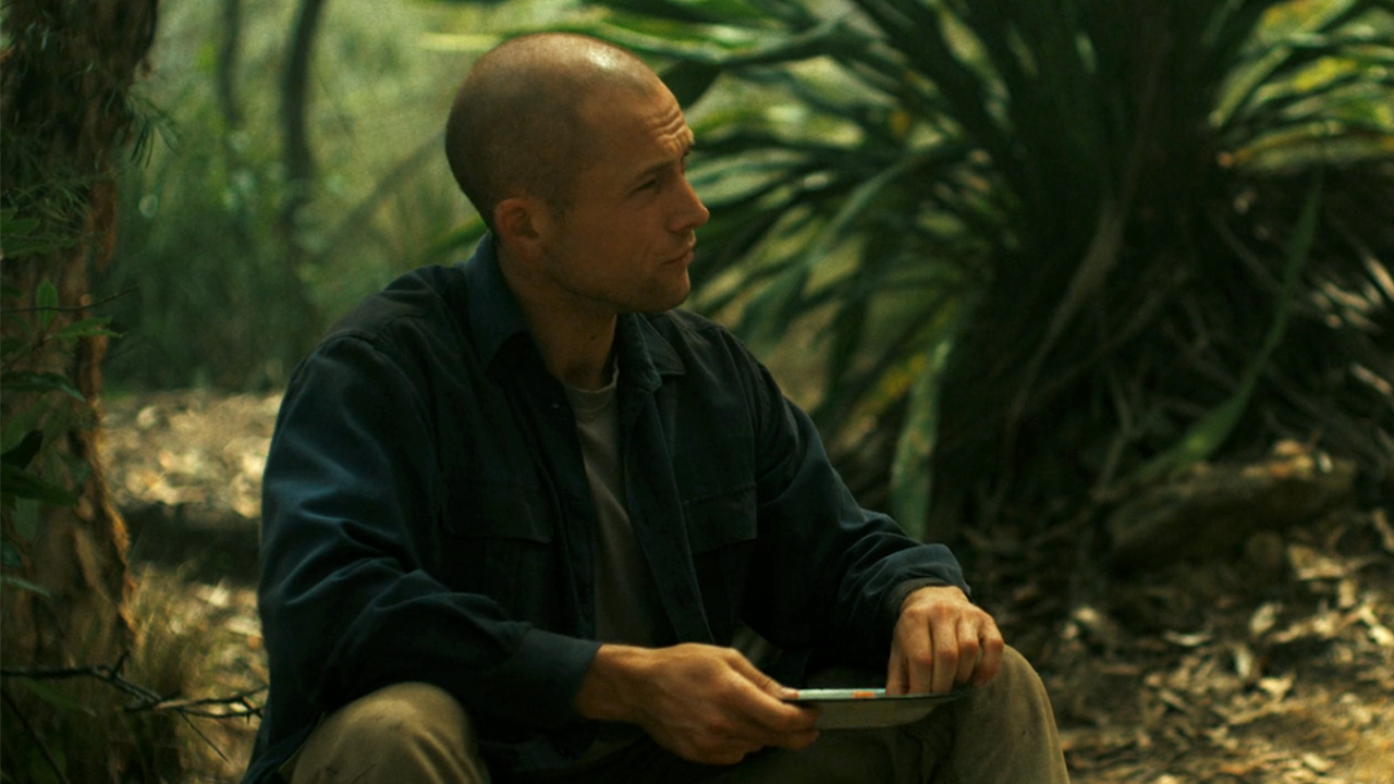 Taron Egerton looking to his left while holding a dish of food in Apex.