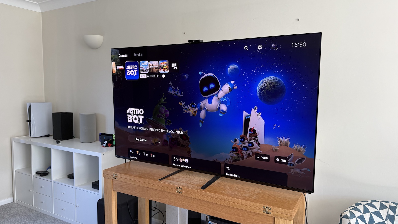 The 65-inch Sony A95L pictured on a wooden table in a living room. On the screen is the PS5 Adjust HDR menus