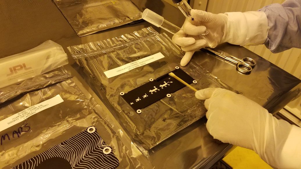 The photo was taken on March 16, 2020 in a cleanroom at NASA&rsquo;s Kennedy Space Center during final preparation for launch. A planetary protection engineer is swabbing and cleaning the surface. This plate features illustrations of all the rovers (and the Mars Helicopter) that have landed on Mars.