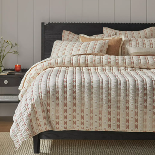 bed with a striped quilt, several pillows, and a black bedframe