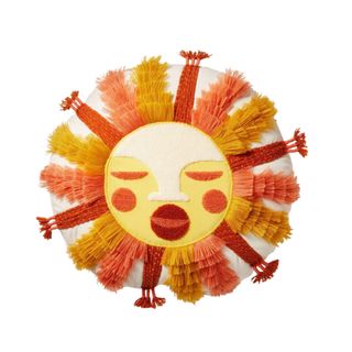 A circular sun throw pillow in red, orange, and yellow, with a face for the sun and fringes for the rays