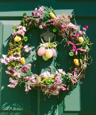 A dark green front door with a colorful floral wreath with ribbons, pink and yellow flowers, green ornaments, and spring chick decorations