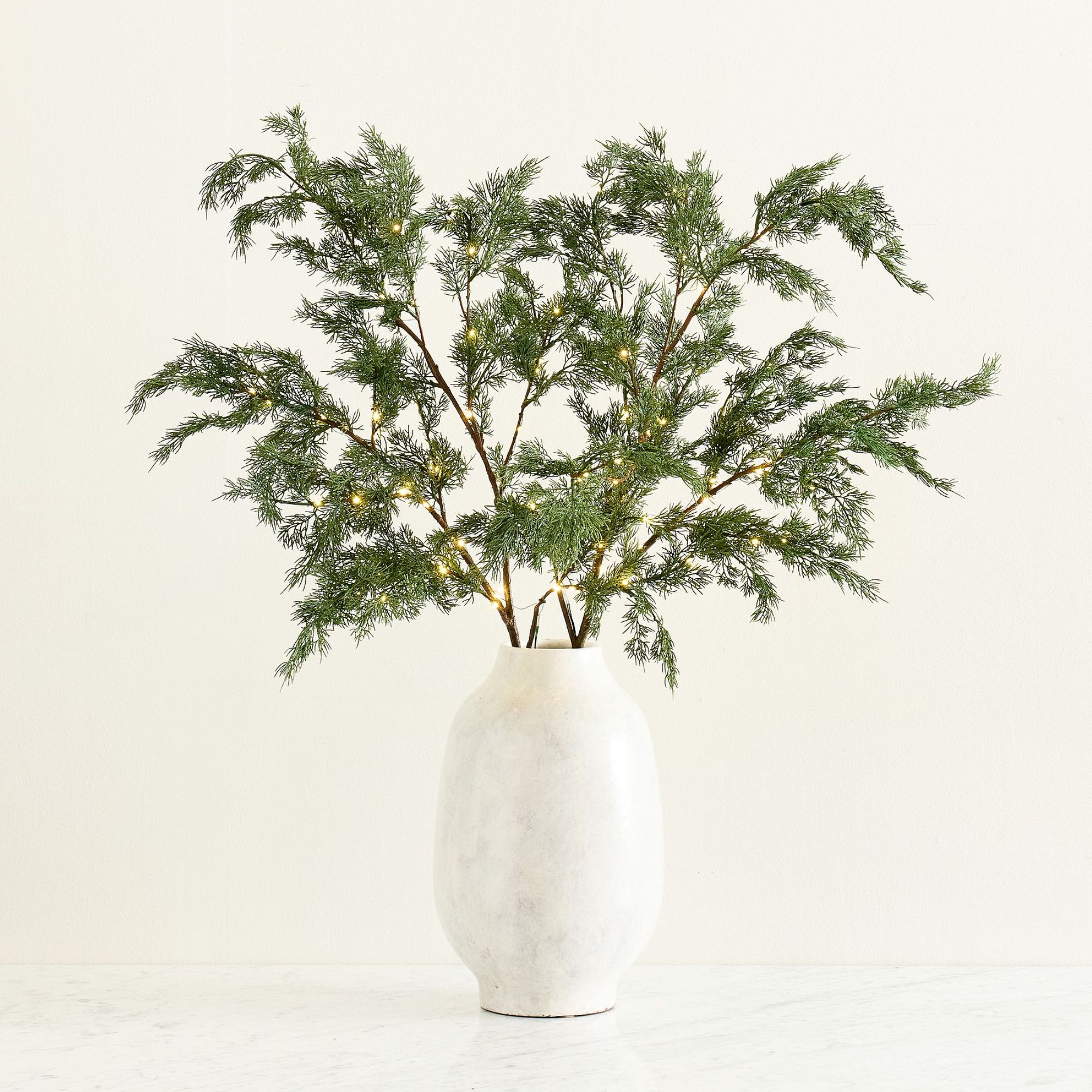 Pre-lit faux cedar branches in white ceramic vase