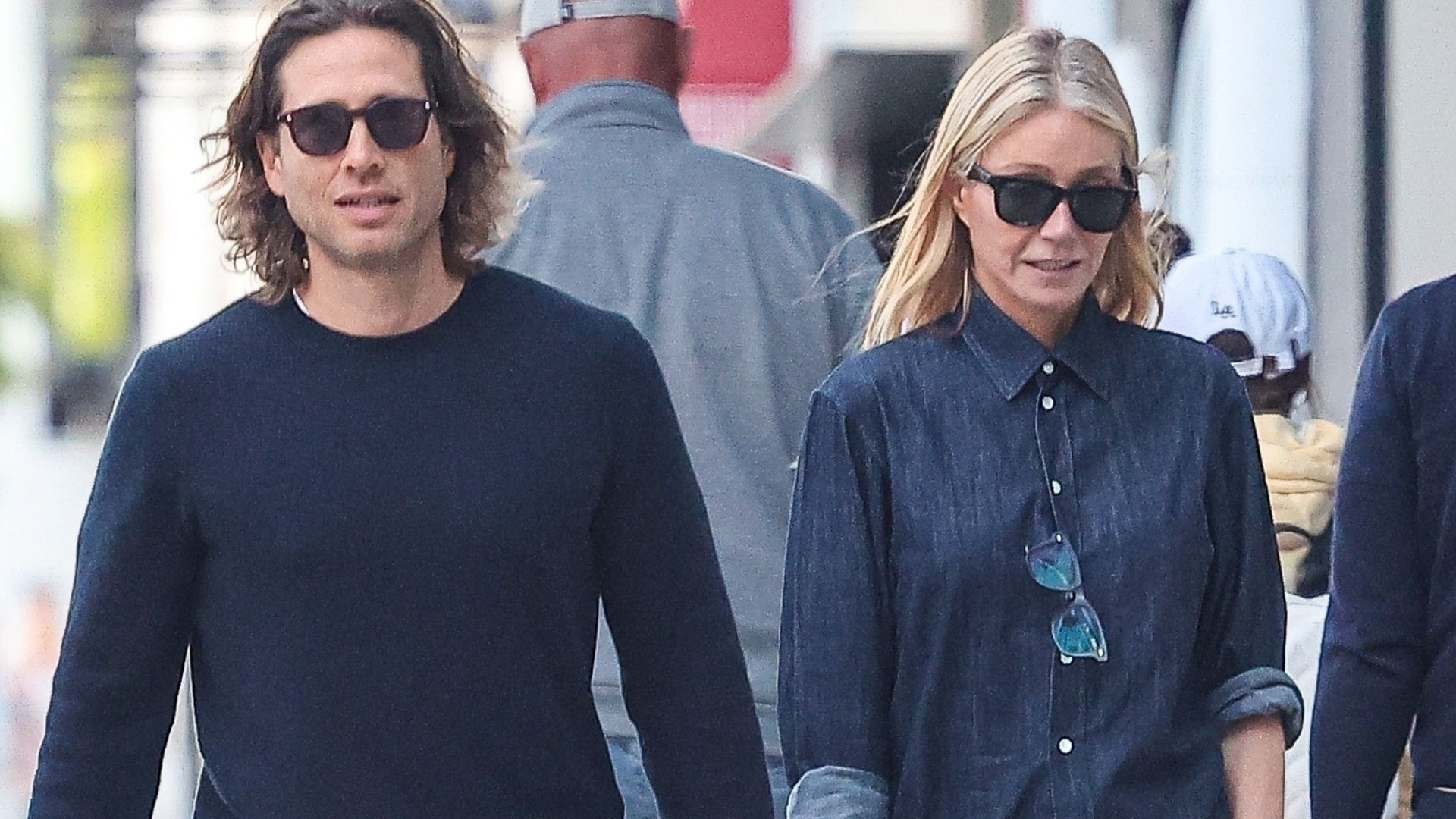 Gwyneth Paltrow walks down the street wearing burgundy trousers with burgundy flats and a denim shirt.