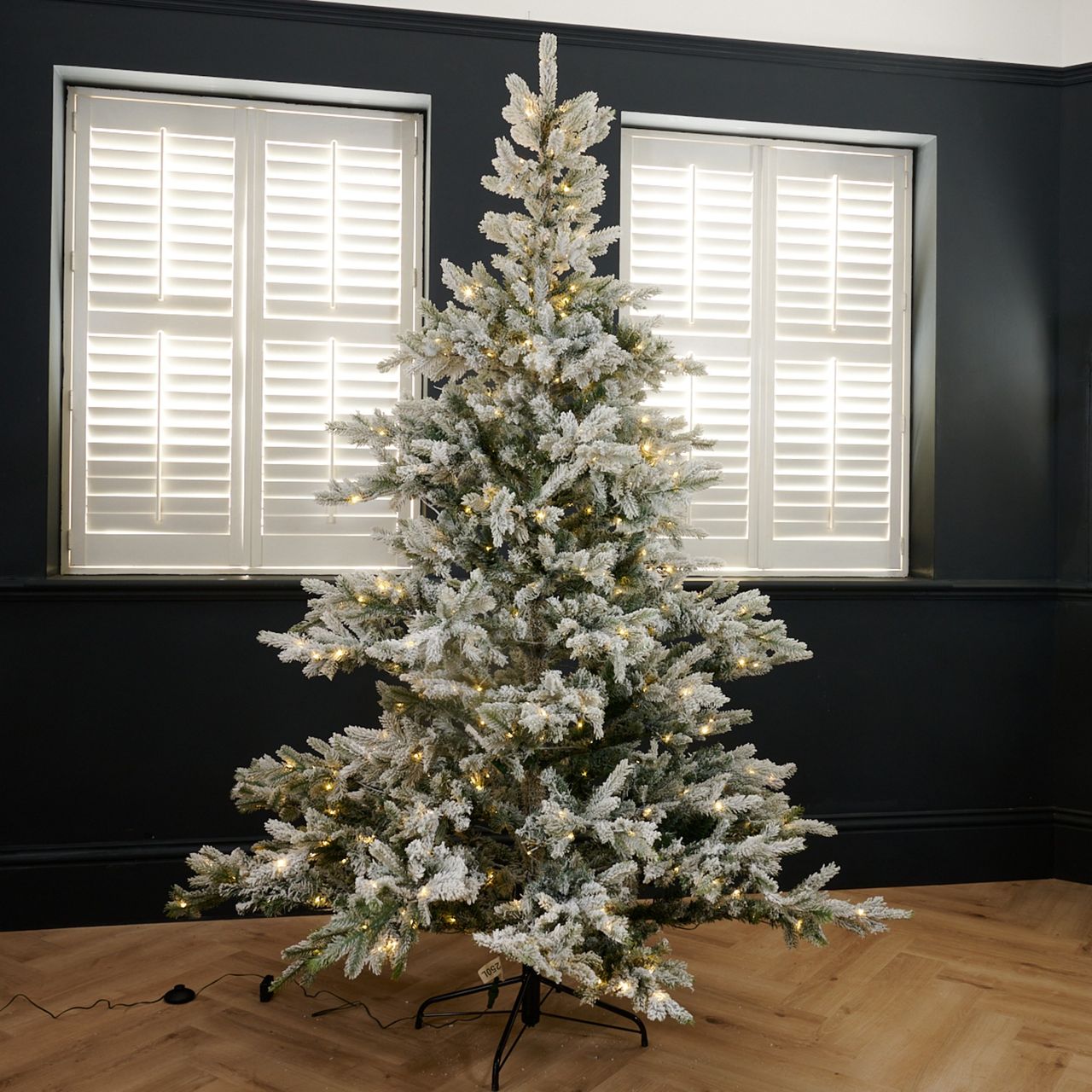 Cox &amp; Cox's Snowy Bergen Spruce Pre-Lit Christmas Tree set up in a black-painted living room