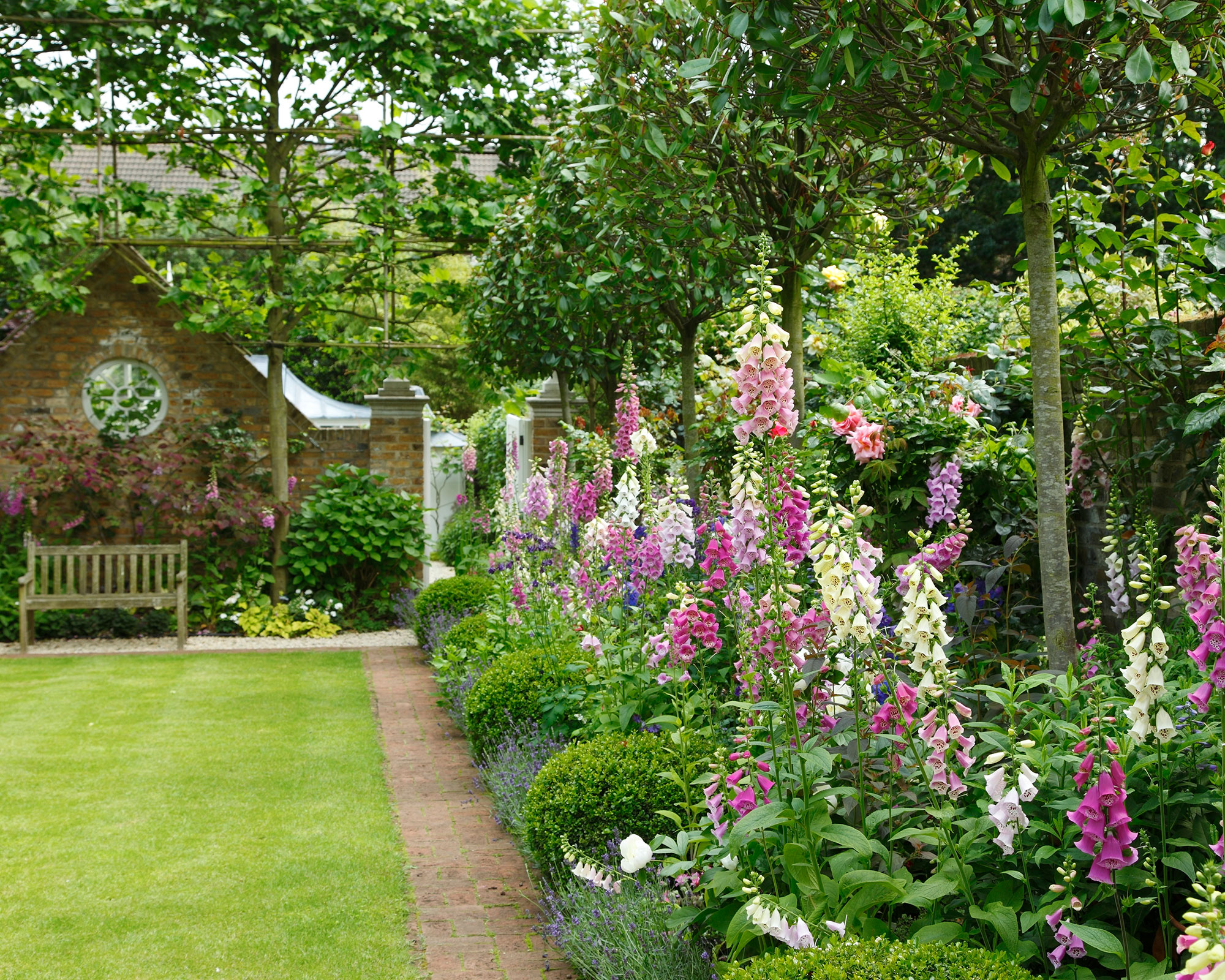 An example of garden shade ideas showing a garden with a lawn and wooden bench next to a large flowerbed