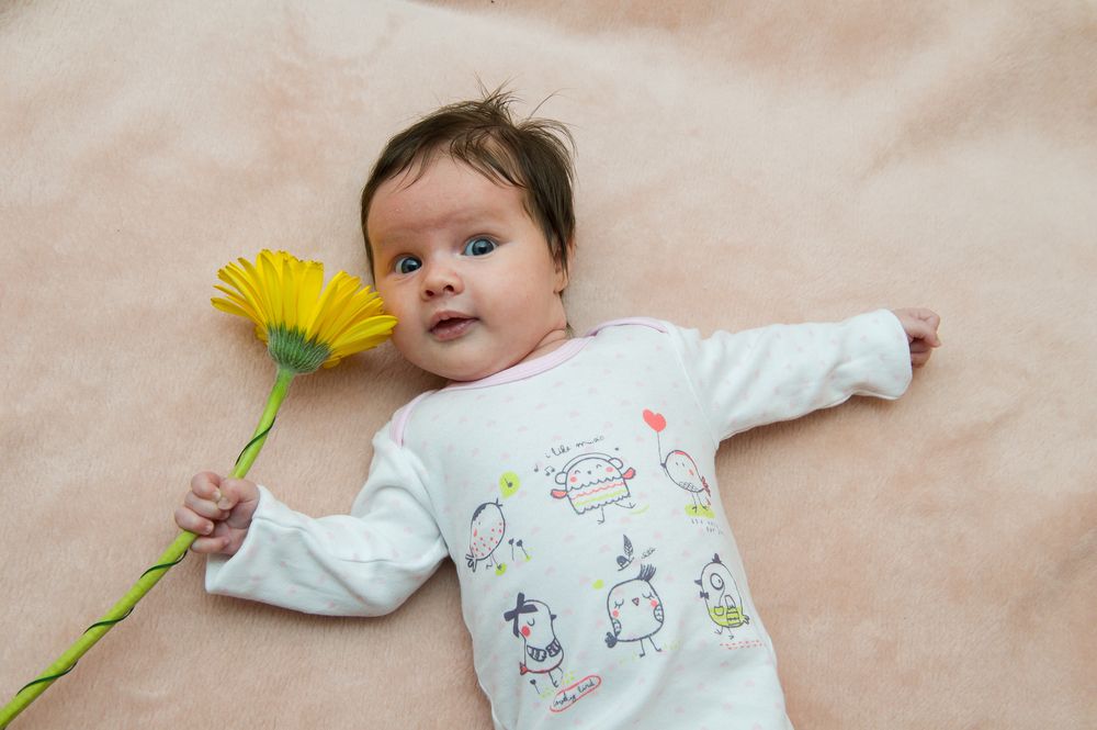 Baby holding a sunflower in her right hand.