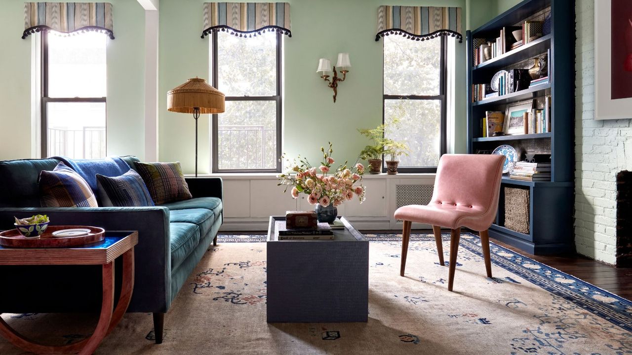 Bright pastel green living room with dark hardwood floors, pale pink and dark blue area rug, velvet blue and pink sofas and slim navy blue bookshelves