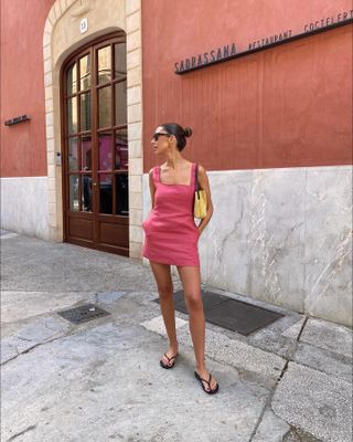 Woman on street wears pink linen mini dress, yellow handbag and black flip flop sandals