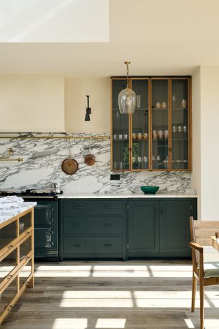 A kitchen with a marble countersplash and glass-fronted upper cabinetry displaying a collection of glassware