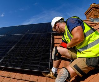 man in hard hat and hi vis jacket on roof working on solar panel installation