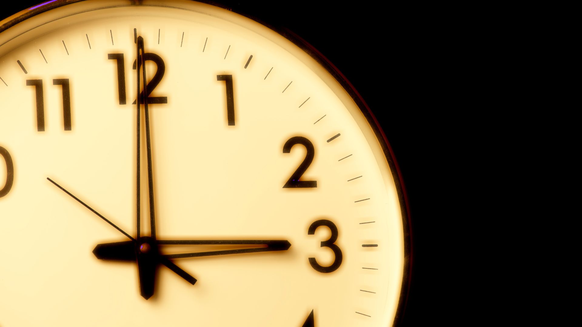 A clock face in the dark showing 3 am in the morning.