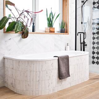 a curved bathtub under a window in a bathroom, clad in marble pencil tiles