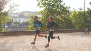 Man and woman running along park track, wearing Brooks running shoes