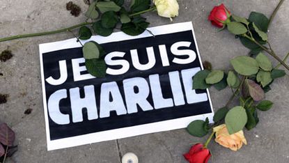 A sign reading "I am Charlie" lies on the ground with roses as people observe a minute of silence in Bordeaux, on January 8, 2015, as they remember the for the victims of an attack by armed g