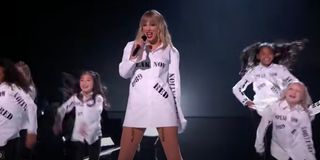 Taylor Swift performing on stage in her album shirt