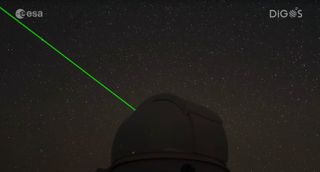 A bright green laser light shines from a darkened dome of an observatory into a starry night sky