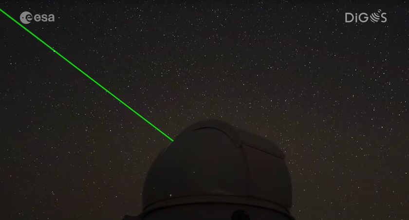 A bright green laser light shines from a darkened dome of an observatory into a starry night sky