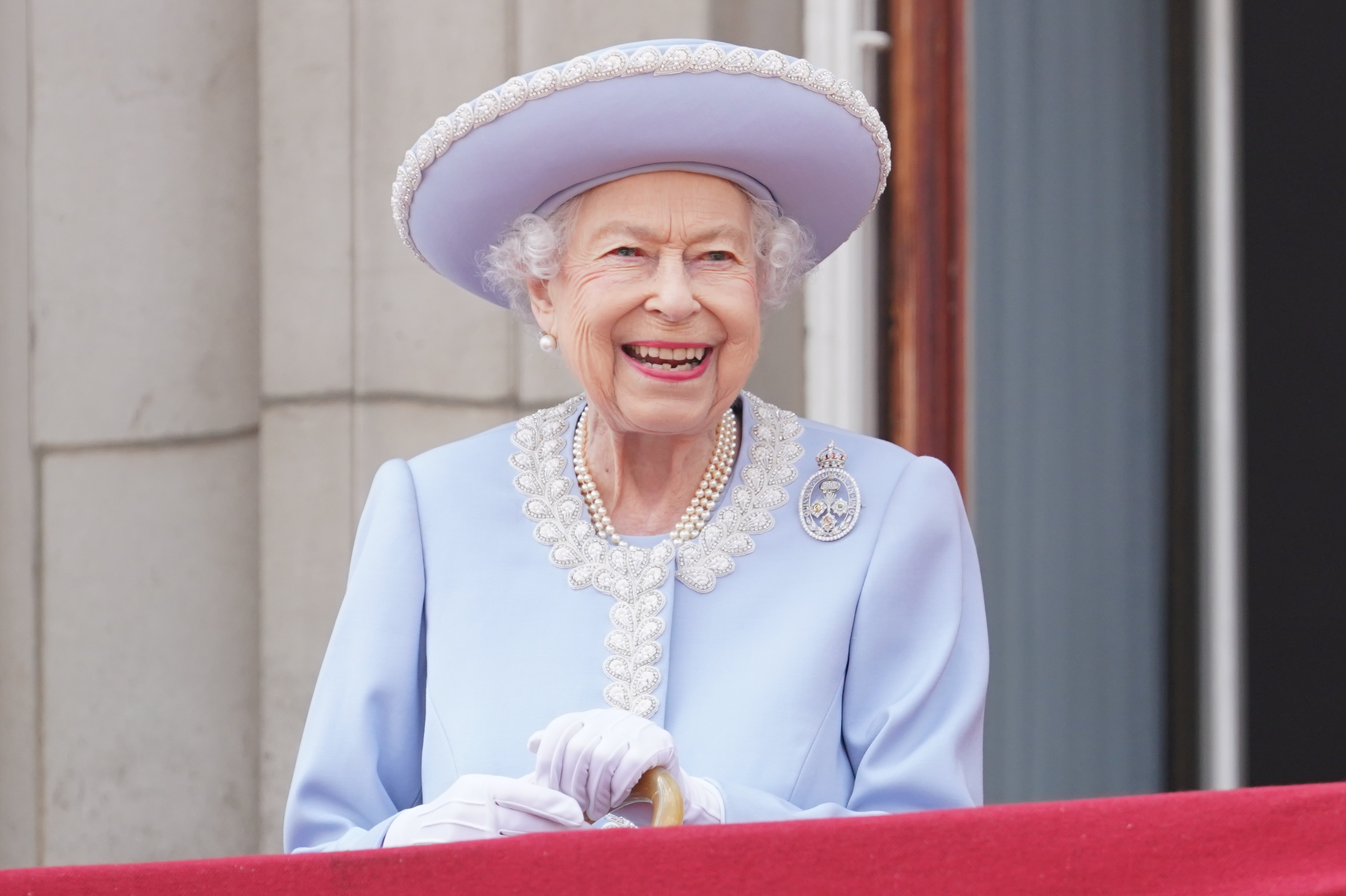 Queen Elizabeth wearing a blue hat and coat and smiling on the balcony of Buckingham Palace