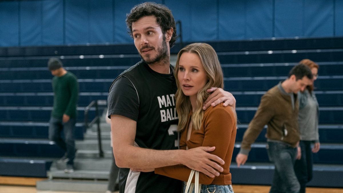 From left to right: Adam Brody and Kristen Bell holding each other while standing in front of bleachers in Nobody Wants This. 