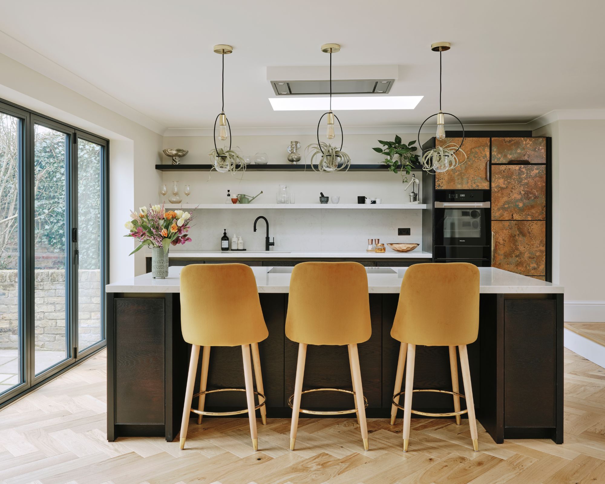 Yellow counter stools line up on black kitchen island with a metal cabinet patina in the background