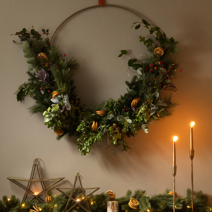 Mantelpiece decorated with foliage, lit candles and star shape candle holders, wreath on wall above.