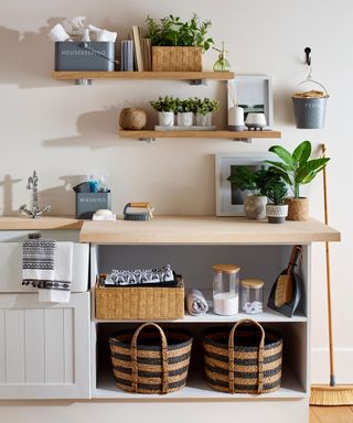 A rustic country kitchen with laundry area by B&M with assortment of woven rectangular and round baskets, broom and indoor houseplants