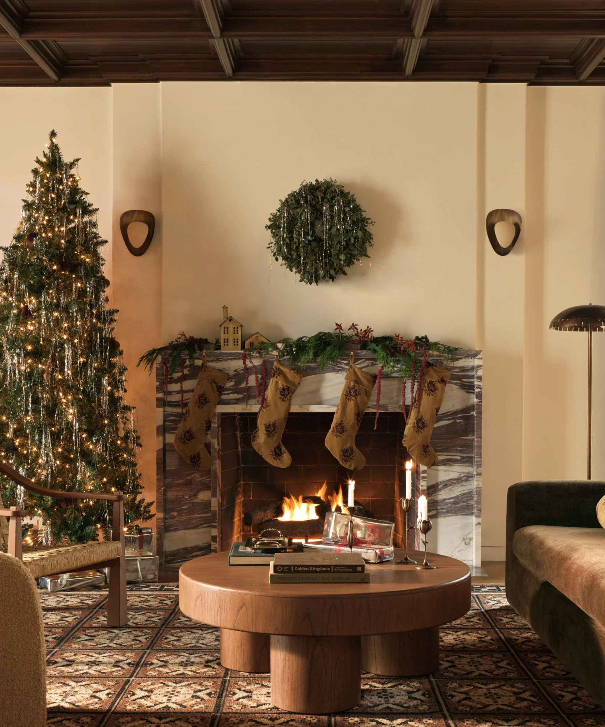 a warm and inviting living room decorated for Christmas with a tree decorated on the left side and a fireplace with stockings hung above and a wreath on the wall above