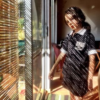 Window blinds cast a striped shadow on girl.