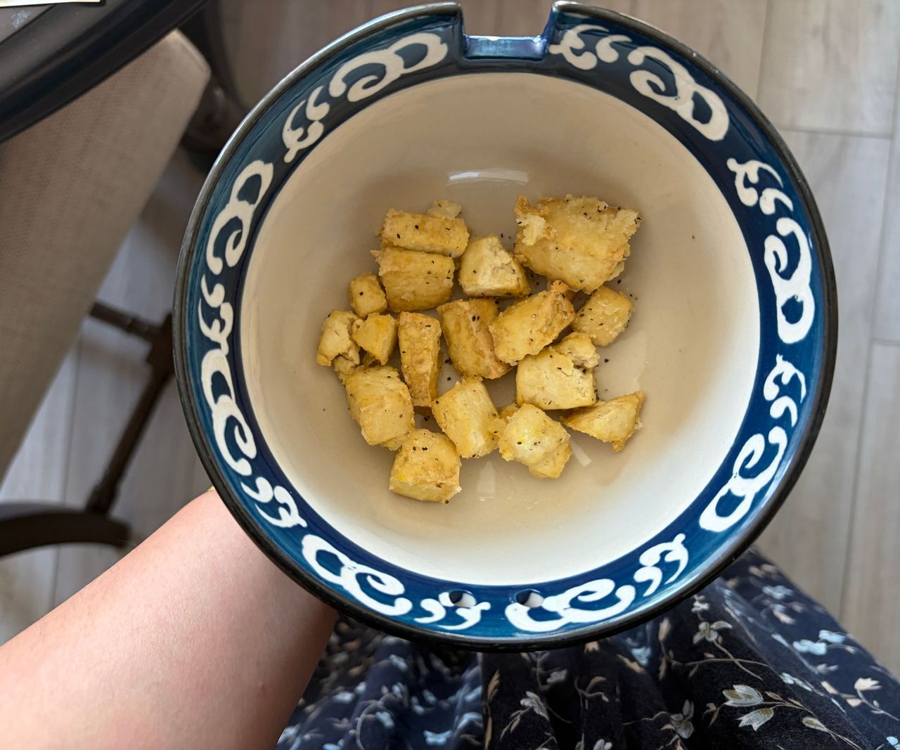 A bowl with a blue painted pattern around the rim with pieces of fried tofu inside.