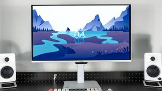 The MSI Pro Max 271UPXW12G monitor on a desk next to a pair of white bookshelf speakers