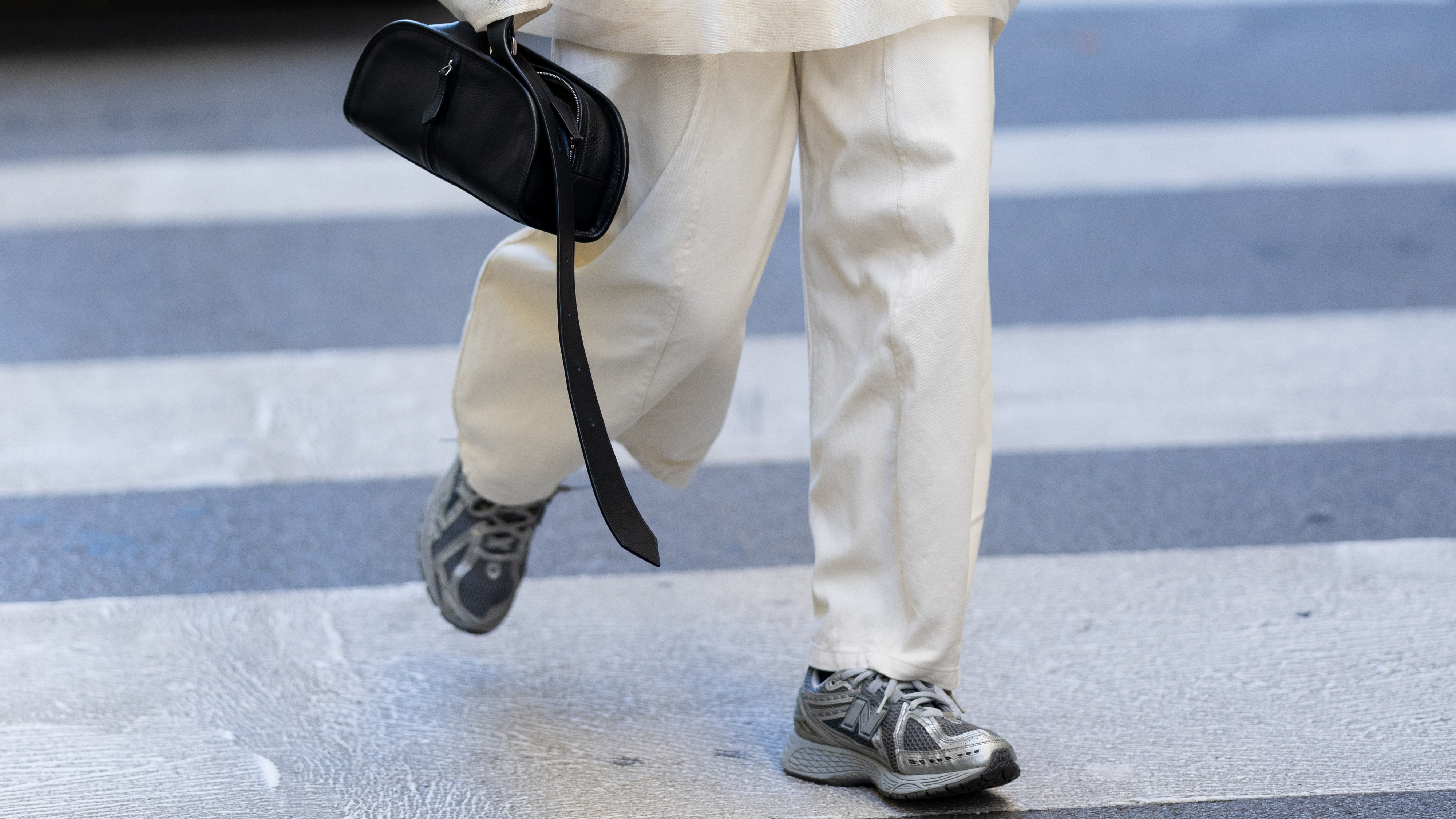 A guest wears silver New Balance sneakers, a black leather bag, a beige turtle neck see-through long sleeved top, a black crop top, a black leather belt and beige high waist trousers outside Calcaterra show during the Milan Fashion Week
