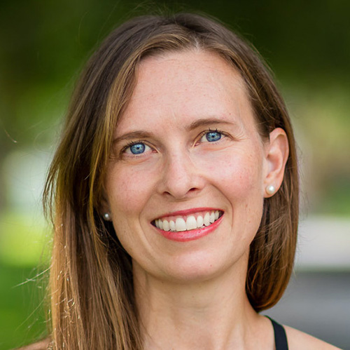 A woman with blue eyes and straight brown hair looks at the camera.