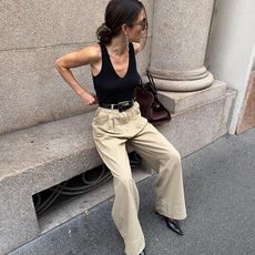 Lida wears black tank and beige colored trousers with pointed boot and brown handbag. 