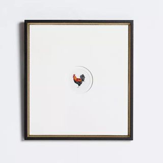 A picture frame with a very small painting of a rooster in the middle