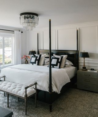 A white bedroom with black four poster bed and a grey Greek key design carpet