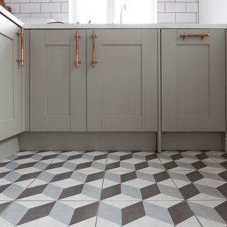 Kitchen with a patterned, cube-design tiled floor and grey cabinets with copper handles