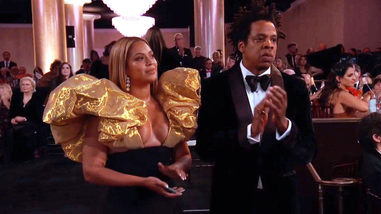 Beyoncé wearing a top with puffy golden sleeves and husband Jay Z.