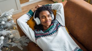 Girl listening to Christmas songs on headphones, relaxing next to the tree